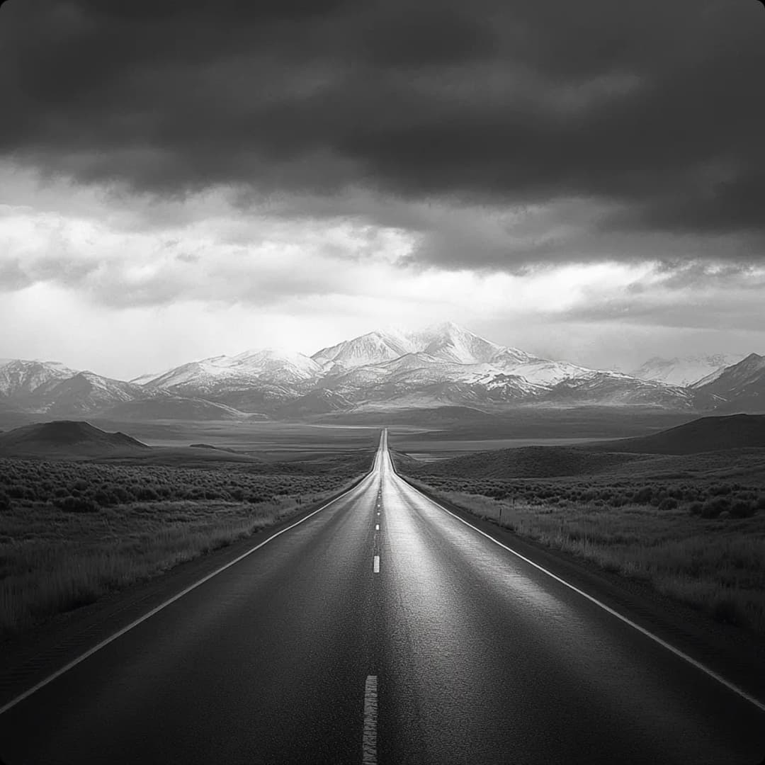 A paved road with fields on the sides leading to a mountain range